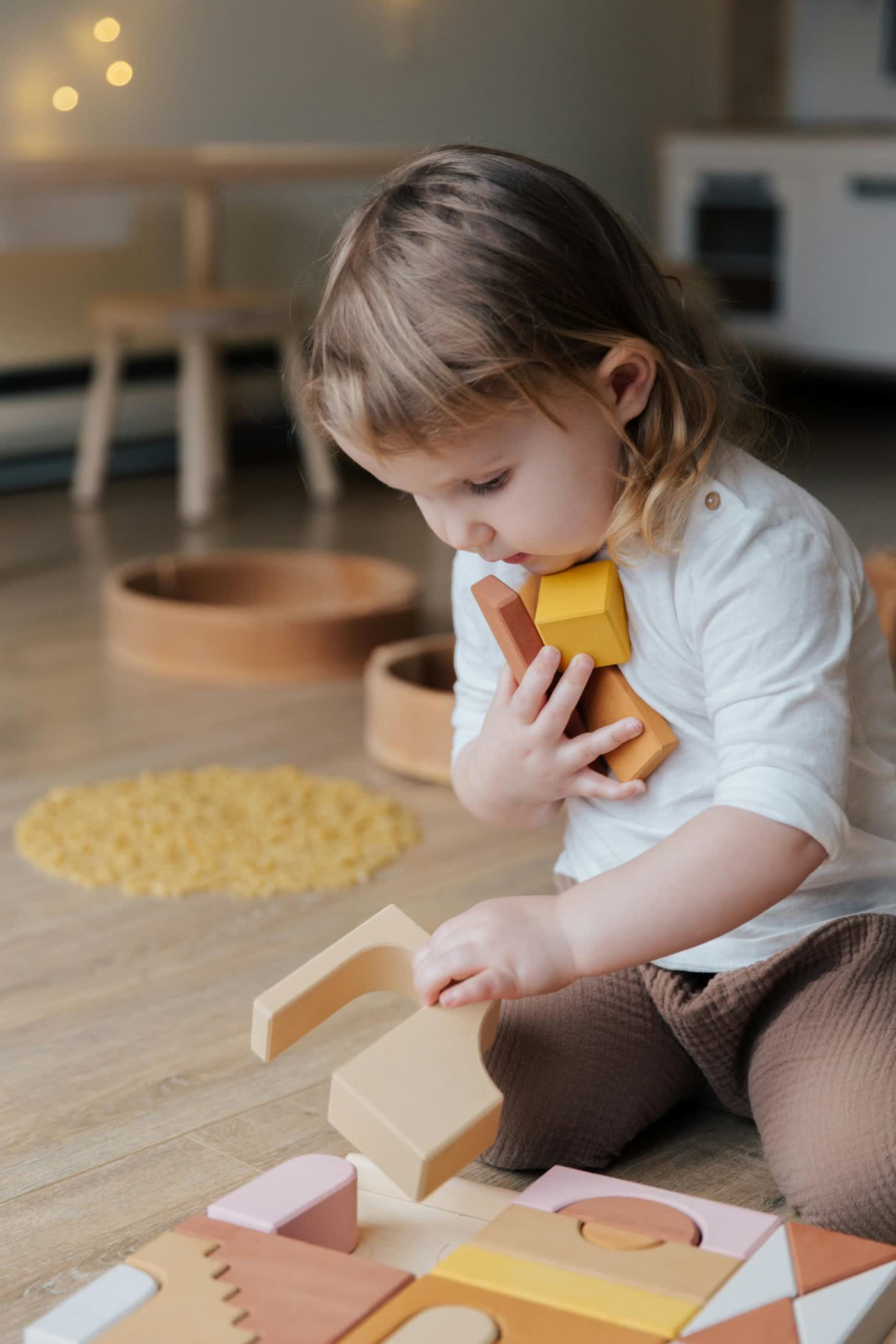 A toddler sitting on the floor building with wooden blocks