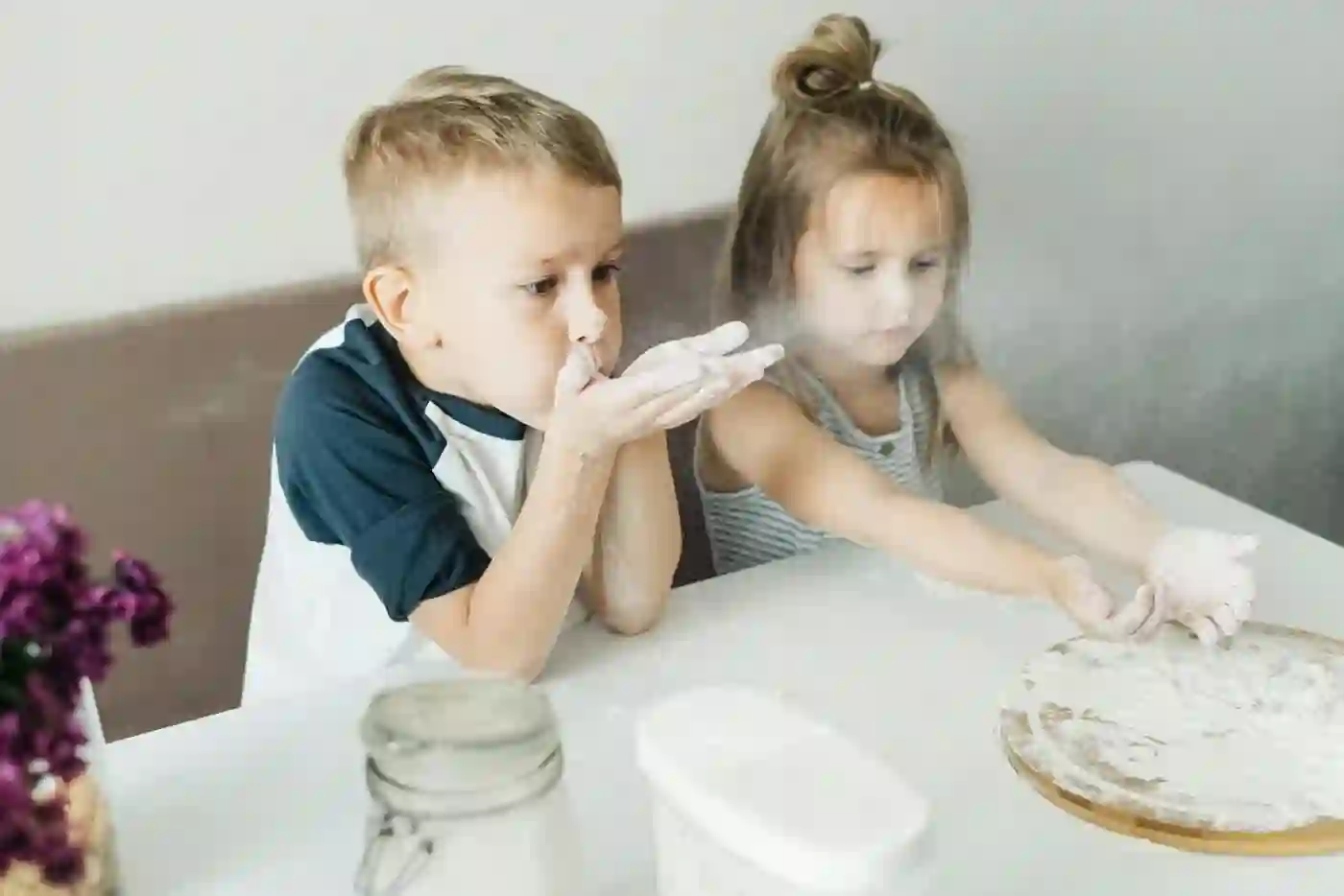 Two children pressing out dough with floury hands at a table