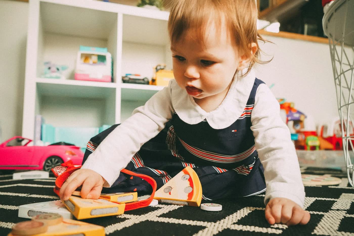A toddler sitting on a rug playing with wooden toy food